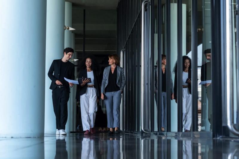 Blick in einen modernen Flur mit Marmorboden und Glasfassaden. Drei Personen in Businesskleidung kommen den Flur entlang.